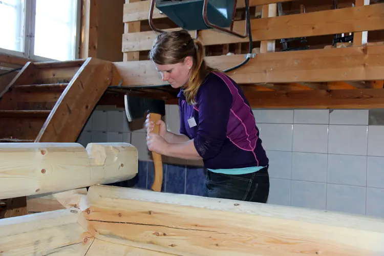 Hege Laugerud hugger et barkelaft i en konstruksjon som ferdigstilt vil fremstå som en gapahuk