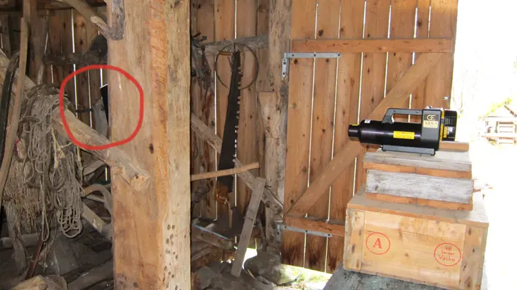 Røntgenundersøkelse av stav i heimeløa, Brudavolltunet, Ørsta. Røntgenrøret sees til høyre i bildet. Litt av billeplaten («filmen») stikker frem bak stolpen og er markert med en rød ring. Skanneren som brukes til å digitalisere («fremkalle») billedplaten står i en bygning med innlagt strøm, like nedenfor heimeløa. Billedplaten må digitaliseres senest 30 minutter etter eksponering for at ikke data skal gå tapt. Foto: NIKU