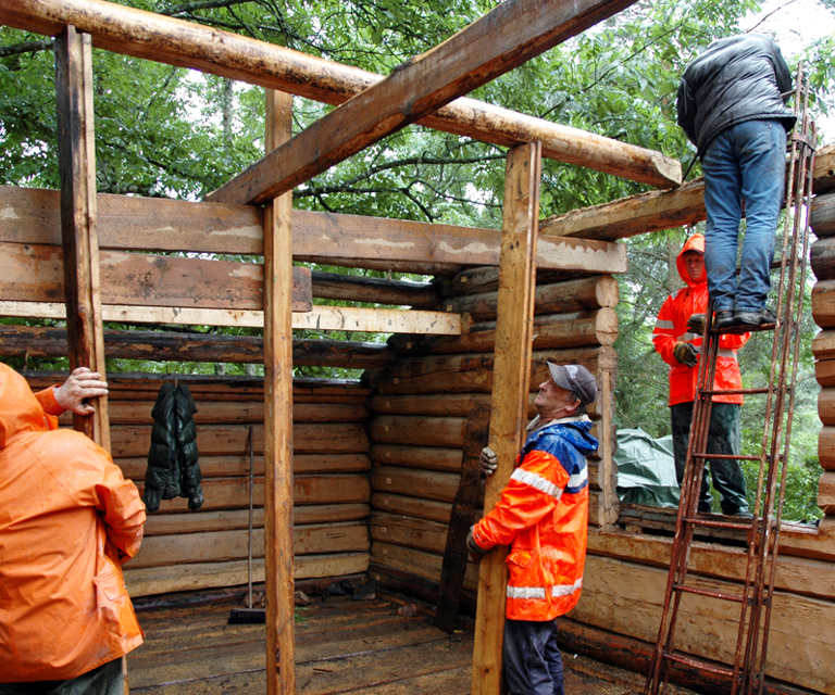 Takåsene støttes opp og vippes ut av sporet. Til denne jobben er det behov for sterke folk. Mye nedbør hele denne sommeren gjorde hverken stokkene eller jobben lettere. Foto: Norske Hjem