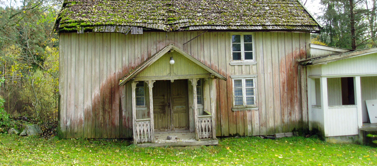 Det gamle svalgangshuset fra slutten av 1700-tallet hadde stått tomt siden 70-tallet og begynte å se svært forfallent ut. Heldigvis viste det seg at skadeomfanget var overkommelig og bygningen kunne reddes. Den eneste måte å redde bygninge på var å flytte den. Til høre ses et nyere tilbygg, dette ble stående igjen på tomta. Sveisterstilveranda ble tilføyd tidlig på 1900-tallet. Utvendig panel, de to vinduene og hovedinngangsdøra er fra rundt 1850. Foto: Norske Hjem
