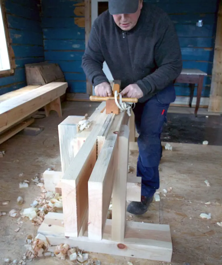 Roald Renmælmo høvlar fjør med ploghøvelen. På kvar side har plogen ein meie som gjer at høvestålet ikkje får ta meir når det når ned på overkant av langborda. Skottbenken er ein noko nedkorta kopi av skottbenken frå Kverndal i Målselv. Foto: Roald Renmælmo