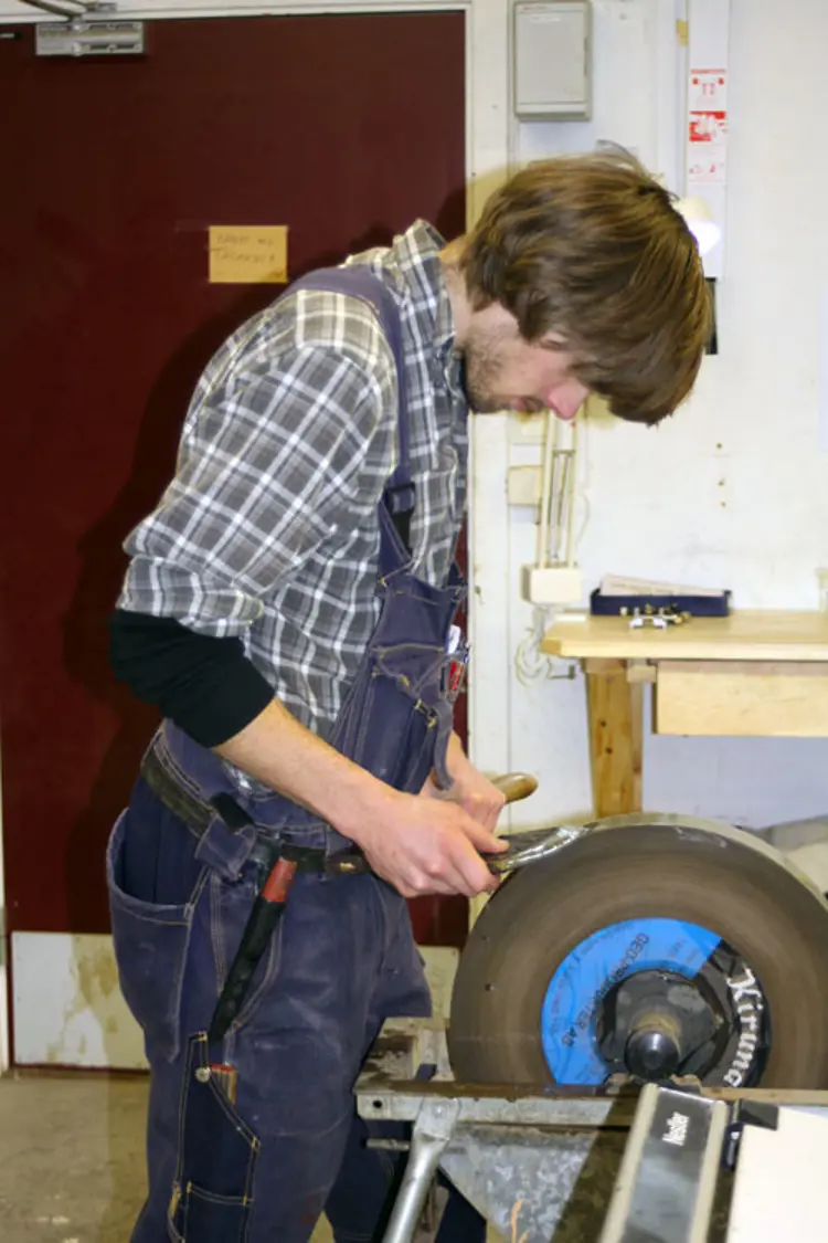Magnus Wammen sliper øksa med elektrisk slipestein. Foto: CEWG