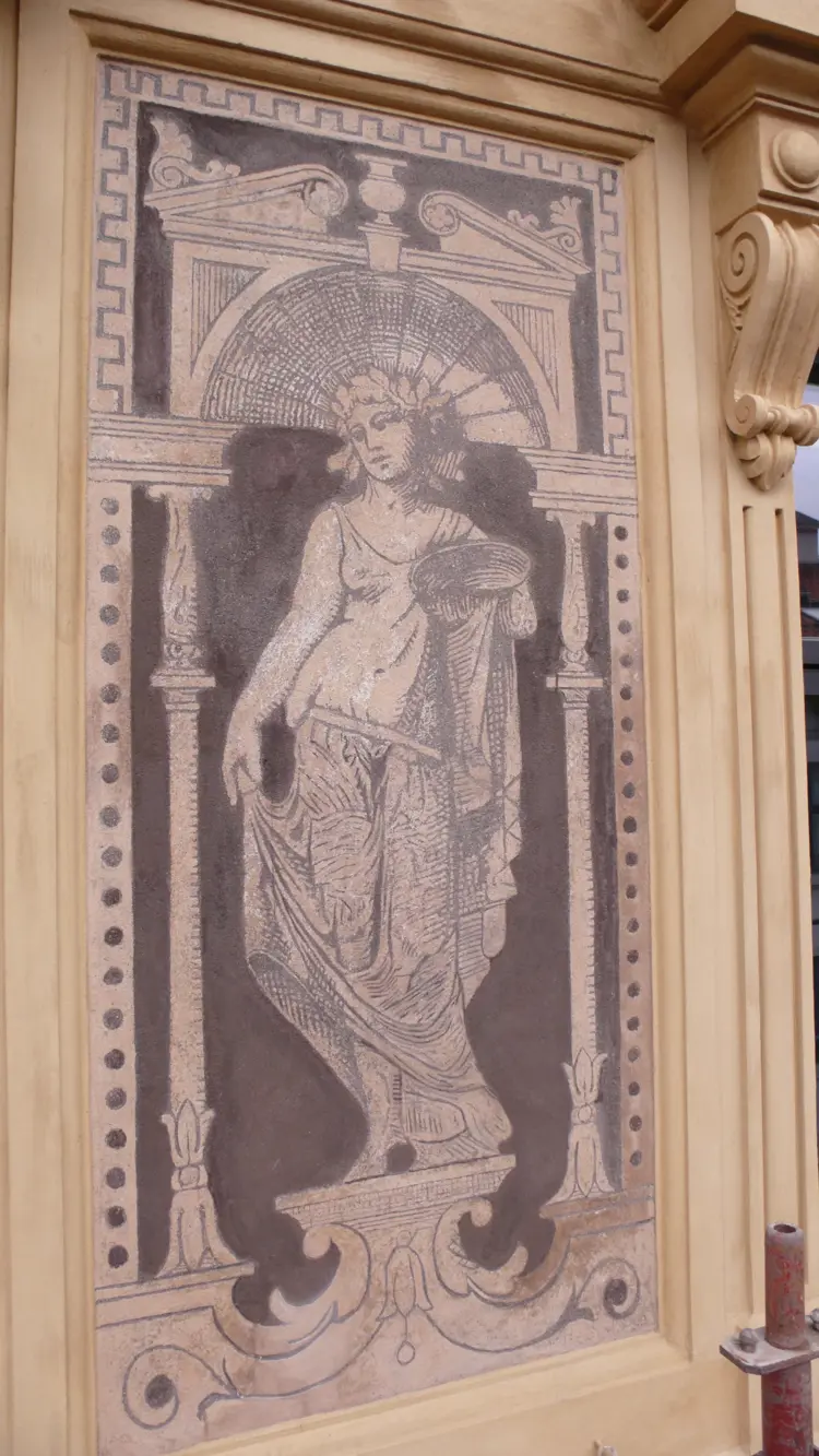 Kvinneskikkelse med skål - kanskje skal den symbolisere jordbruket eller servering? Motivet er rammet inn av en portal bastående av et brudt tympanon (tempelgavl) med en sareptakrukke og akantusløv, støttet av søyler. 