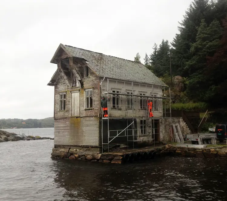 Sånn så hovedhuset i Solstrand handelssted ut ved kjøp, det var nok å ta fatt på. Det var mye råte. Oppover i huset var det skader etter lekkasjer fra vinduer og dører, på vegger og i golv. En vegg var slått inn i en storm, den måtte skiftes i sin helhet. Kun tre vinduer mot nord kunne reddes. Foto: Lise Bjelland